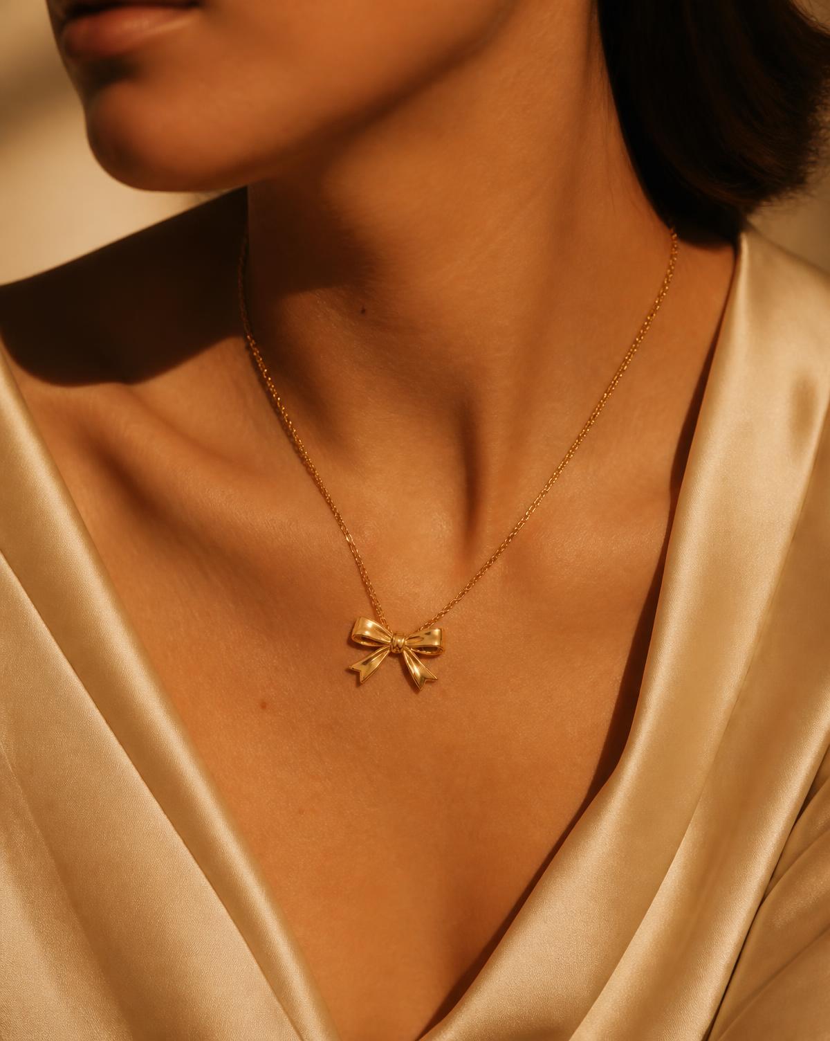 Gold bow pendant necklace worn on ivory silk